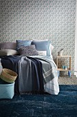 Blankets in various shades of blue on bed against wall with white and blue patterned wallpaper
