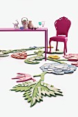 Pinkfarben lackierter Rokokostuhl, lila Tisch mit Nippes Sammlung und florale Filzkreationen auf dem Boden