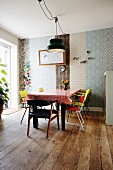 Dining area with colourful, retro chairs around table, wall decorated with strips of various wallpapers and rustic wooden floor