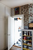 Glass-fronted cabinet against wall with strips of wallpaper in different patterns and open door leading into kitchen
