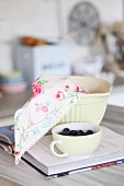 Cup of fresh blueberries and floral cloth in mixing bowl on recipe book