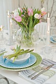 Pastel place setting with asparagus spears and glass vase of tulips on festively set table
