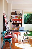 Black desk on trestles, colourful wooden chairs, ornaments on bookcase and open window in background