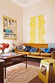 Yellow and wooden 70s retro furniture, yellow painting on wall above sofa with blue-patterned cushion
