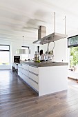 Designer island counter below extractor hood in open-plan kitchen with white, wood-beamed ceiling