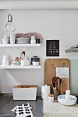 Crockery on white floating shelves above bread bin and kitchen utensils