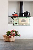 Bouquet of proteas in basket on concrete floor in front of saucepans on vintage, wood-fired cooker in niche