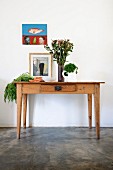 Ländlicher Holztisch mit Gemüse und Blumenvase, vor Wand mit aufgehängtem Bild