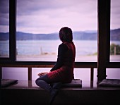 Woman sitting on window seat next to glass wall