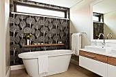 Freistehende Badewanne vor Wand mit Oberlicht-Fenster und schwarz-weißer Tapete mit Baummuster in Designerbad