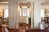 View from foyer into hall with white wooden columns and stained glass front door; partial views into living and dining areas in elegantly renovate cottage