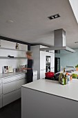 Woman in open-plan kitchen with free-standing counter and hob beneath extractor hood