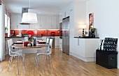 Festively set, oval dining table and shell chairs in open-plan, white, fitted kitchen with red splashback