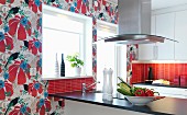 Fitted kitchen with red, tiled splashback and colourful wallpaper