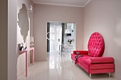 Deep pink couch with round backrest and pale pink console table below mirror in elegant modern foyer