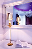 Gold-coloured, elegant table lamp in front of hand-crafted mirror in glamorous bedroom