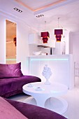 Atmospherically lit, white kitchen counter with purple pendant lamps in elegant, open-plan living area