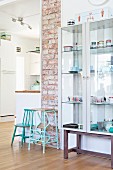 Retro child's chair and step stool painted turquoise against strip of exposed brickwork and next to crockery in glass display case
