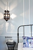 Moroccan-style pendant lamp casting pattern of light on wall next to metal lattice headboard of metal bed