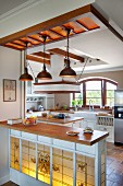 Wooden kitchen counter with backlit, traditional-style, stained-glass panel on front below rustic pendant lamps in open-plan, country-house kitchen