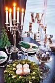 Adventskranz und mehrarmiger Kerzenleuchter mit brennenden Kerzen auf gedecktem Tisch