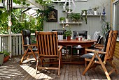 Wooden chairs with black seat cushions around table on veranda with wooden floor