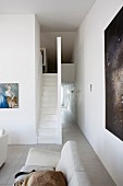 Teilweise sichtbares Sofa in offenem Wohnraum, im Hintergrund Treppenaufgang mit minimalistischem Flair