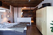 Schlafbereich mit rustikaler Holzbalkendecke, weißen Spindschränken und Bad Ensuite in Loft-Wohnung