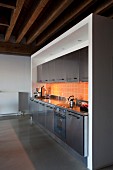 Stainless steel kitchen counter with orange wall tiles in loft apartment with rustic, wood-beamed ceiling