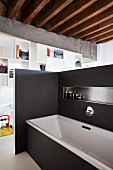 Bathtub screened by black partition wall with integrated shelf and white partition shelving in background in loft apartment