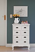 Jug of roses on white, country-house-style chest of drawers below picture on grey-painted wall