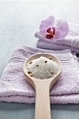 Wooden spoon of bath salts and orchid on lilac towels