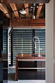 Detail of sink in counter in front of floor-to-ceiling windows with closed louver blinds below wood-beamed ceiling