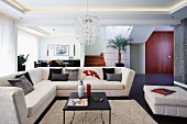 Elegant, pale corner couch and coffee table on flokati-style rug in open-plan interior with indirect ceiling lights