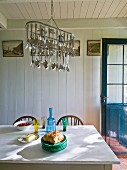 Crockery on table below pendant lamp decorated with cutlery in rustic dining room with wooden walls and ceiling painted white
