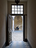 Open, historical front door with diamond-chequered floor tiles and view into cobbled courtyard