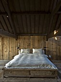 Double bed with white bed linen in minimalist, wood-clad bedroom with rustic ambiance