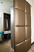 Open, upholstered sliding door with brown, shimmering cover and view into dressing room