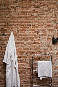Dressing gown hung on brick wall next to chrome towel rail