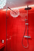 Rainfall shower and hand-held shower head on red tiled wall with reflection of pendant lamp