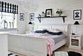 White, antique wooden bed below black shelf on wooden wall and table lamps on bedside cabinets in rustic bedroom