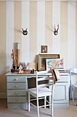 Desk and chair below hunting trophies hung on striped wallpaper