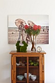 Artistic photo above pair of rabbit ornaments. vase of proteas and retro alarm clock on top of small glass-fronted cabinet