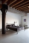 Schwarzes Metallbett mit schwarzer Bettwäsche in minimalistischem Schlafbereich einer Loftwohnung, rustikale Holzdeckenkonstruktion