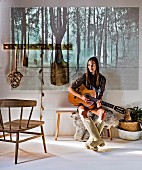 Young woman holding guitar sitting on bench; picture of forest projected on wall