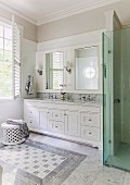 Fitted washstand, white base cabinets, mirrored wall units with sconce lamps and glazed shower area in elegant bathroom