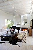 Stühle mit Tierfell und weisses Sofa um Couchtisch, im Hintergrund Klavierflügel neben Kamin im Wohnzimmer