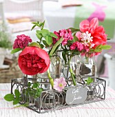 Retro milk bottles used as vases for peonies and other garden flowers in ornamental, grey wire bottle carrier