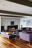 Elegant, purple sofa set in lounge area with arc lamp and cosy open fire in stone wall