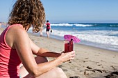 Woman sitting on beach holding glass of juice